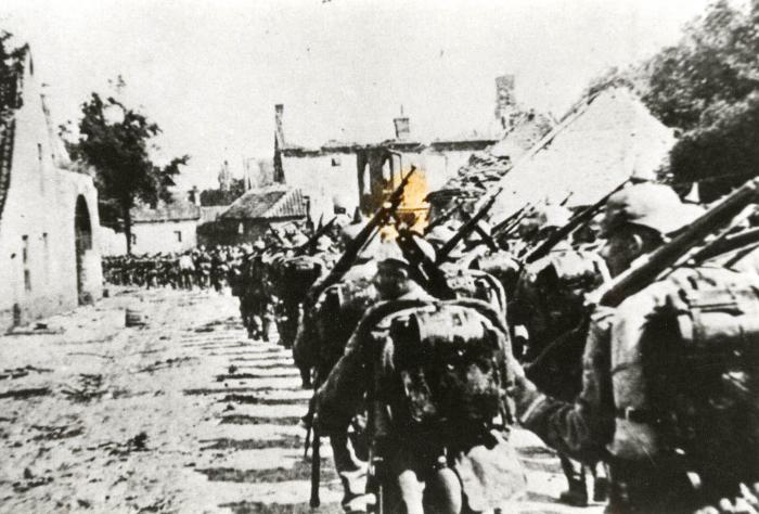 Duitse soldaten marcheren langs vernielde huizen