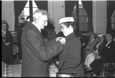 Huldiging gedecoreerden Unions: burgemeester speldt het ereteken op bij een mevrouw, Izegem 1957