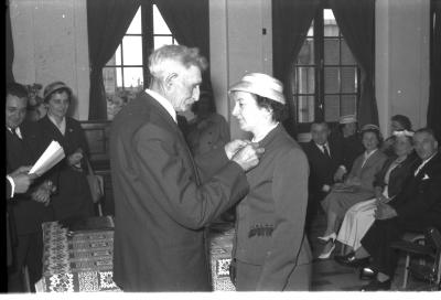 Huldiging gedecoreerden Unions: burgemeester speldt het ereteken op bij mevrouw J. Remmerie, Izegem 1957
