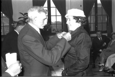 Huldiging gedecoreerden Unions: burgemeester speldt het ereteken op bij een mevrouw, Izegem 1957