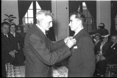 Huldiging gedecoreerden Unions: burgemeester speldt het ereteken op bij een mijnheer, Izegem 1957