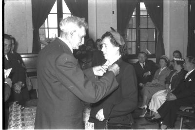 Huldiging gedecoreerden Unions: burgemeester speldt het ereteken op bij een mevrouw, Izegem 1957