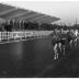 Fotoreportage atletiekwedstrijd: atleten lopen voorbij tribune, Izegem 1957