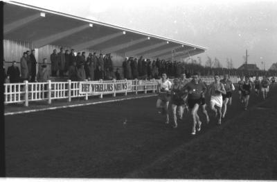 Fotoreportage atletiekwedstrijd: atleten lopen voorbij tribune, Izegem 1957